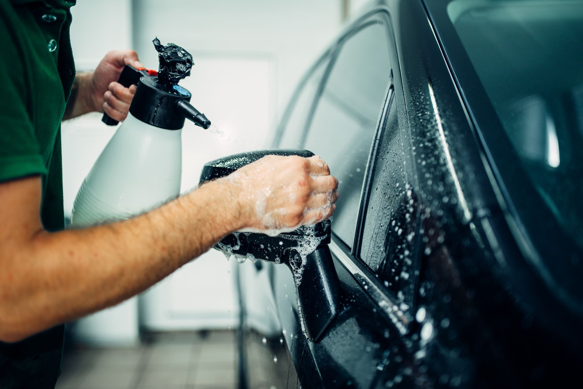 A man is washing a car with a spray bottle.