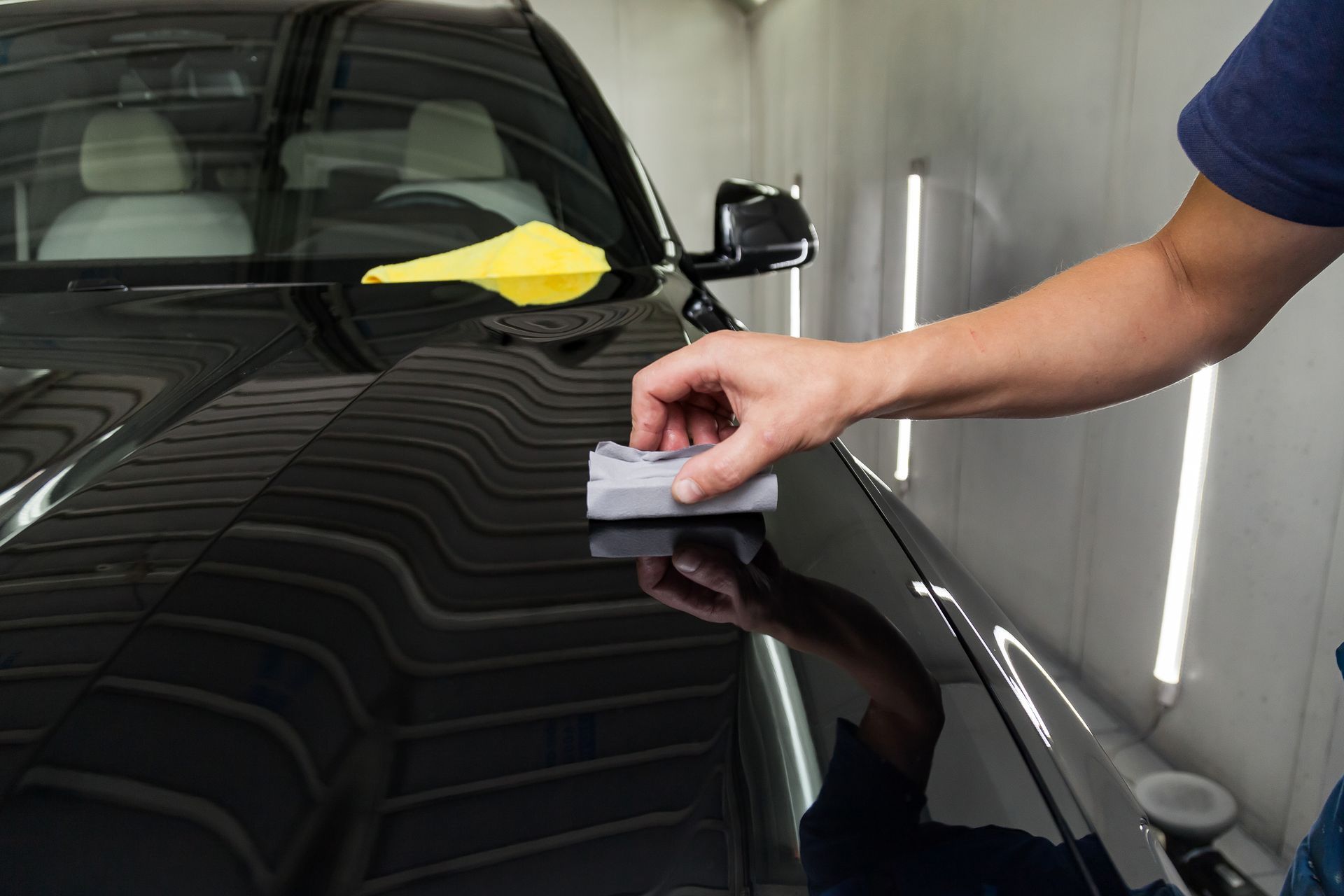 A person is polishing the hood of a black car.