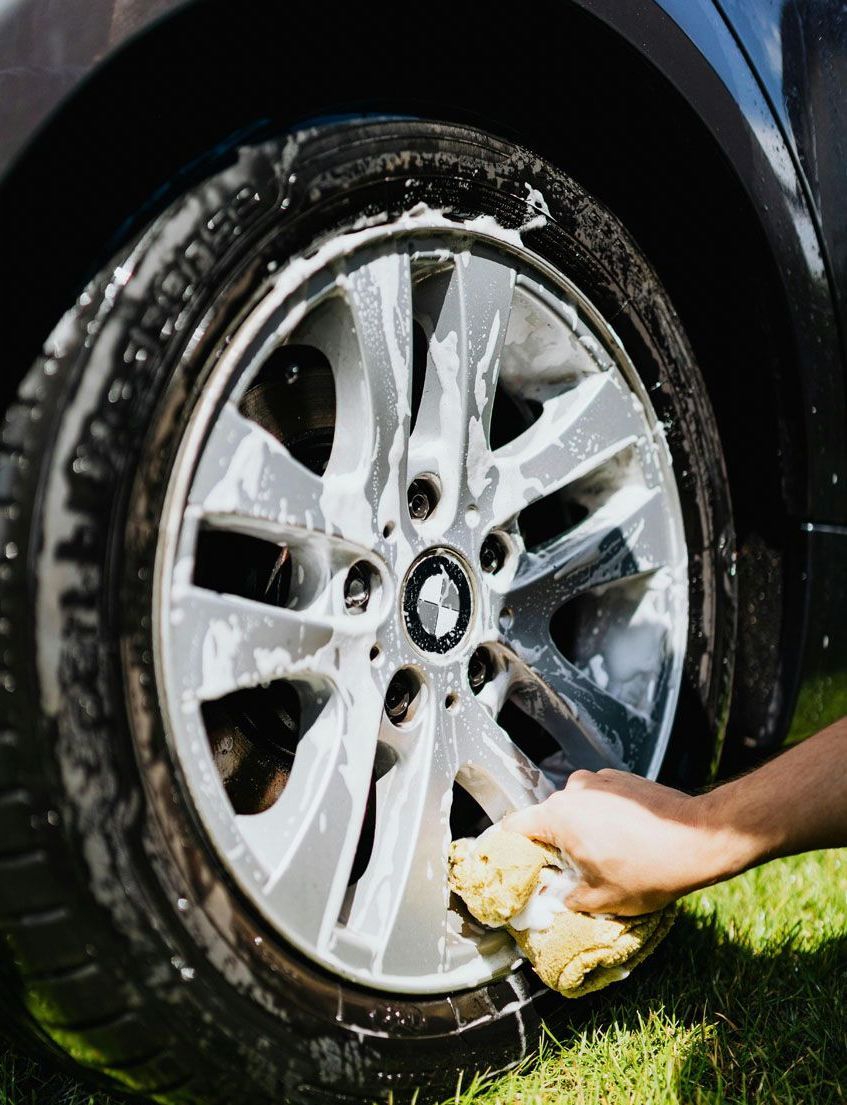 A person is washing a car wheel with a sponge.