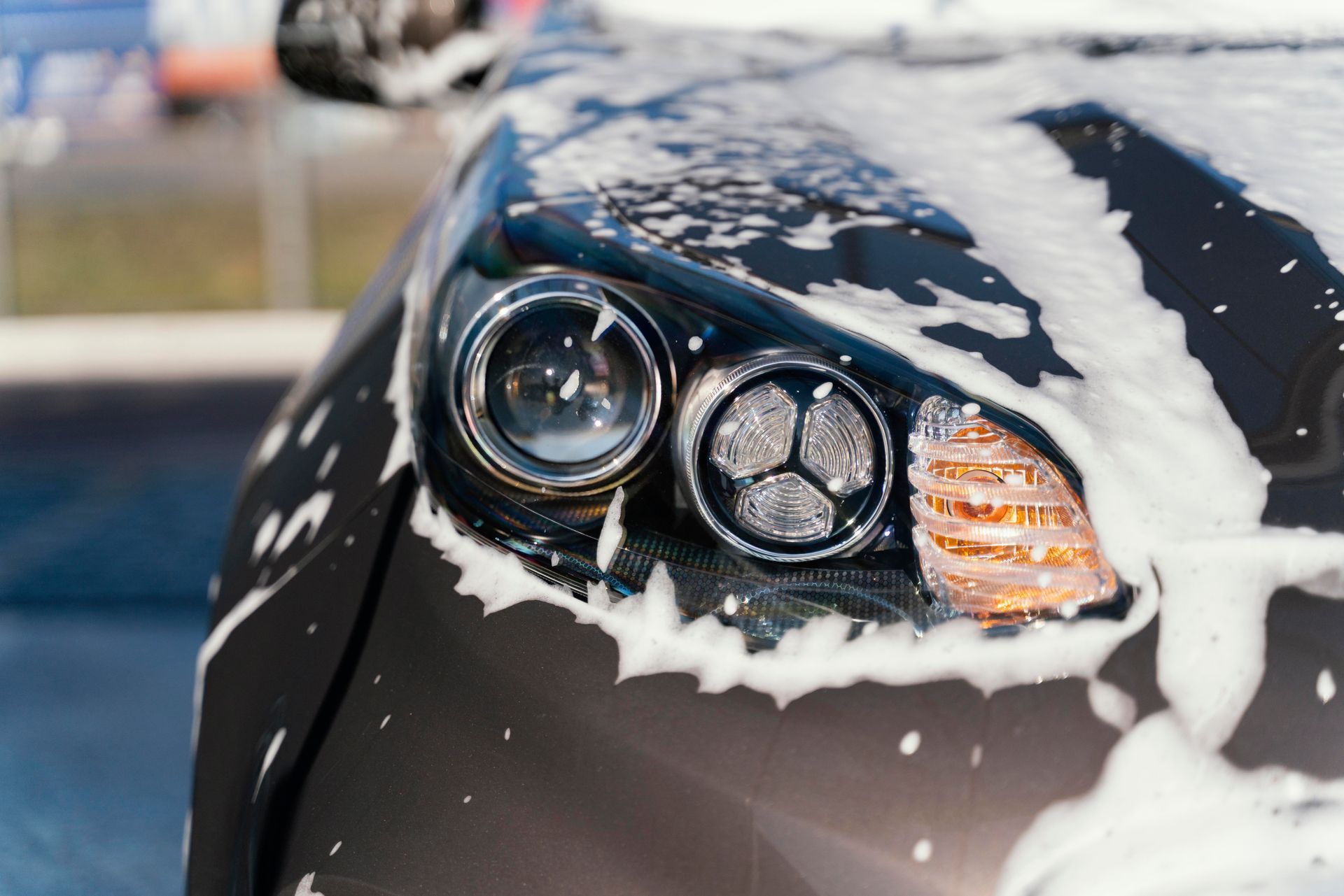 The headlights of a black car are covered in foam.
