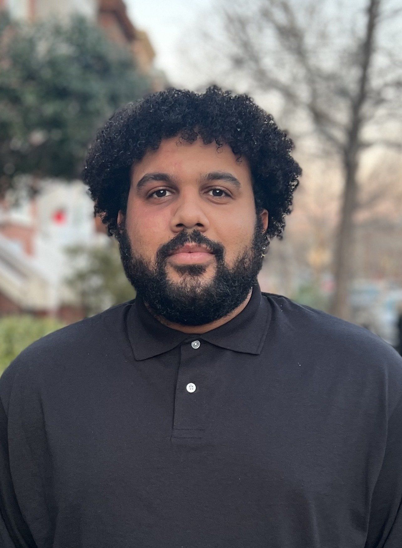 A man with a beard and curly hair is wearing a black polo shirt.