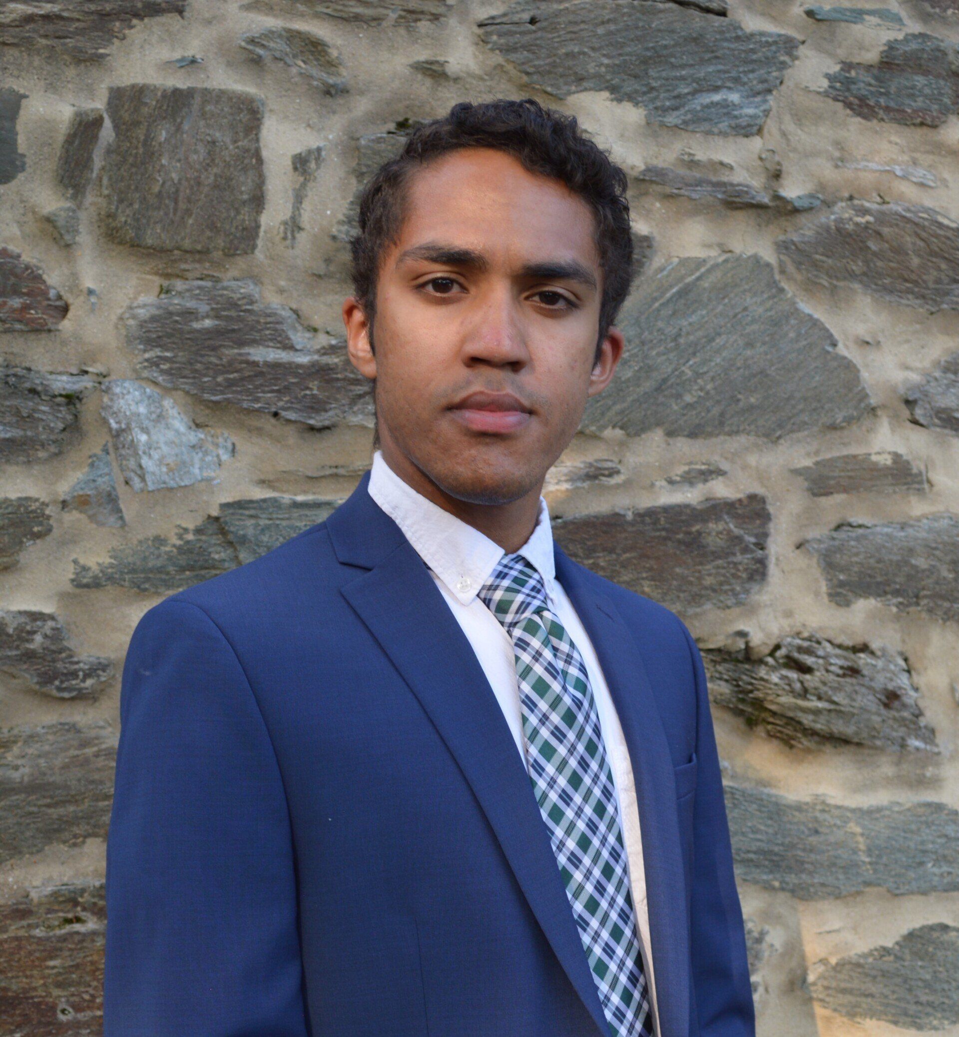 A man in a suit and tie is standing in front of a stone wall.