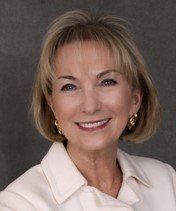 A woman wearing a white jacket and earrings is smiling for the camera.