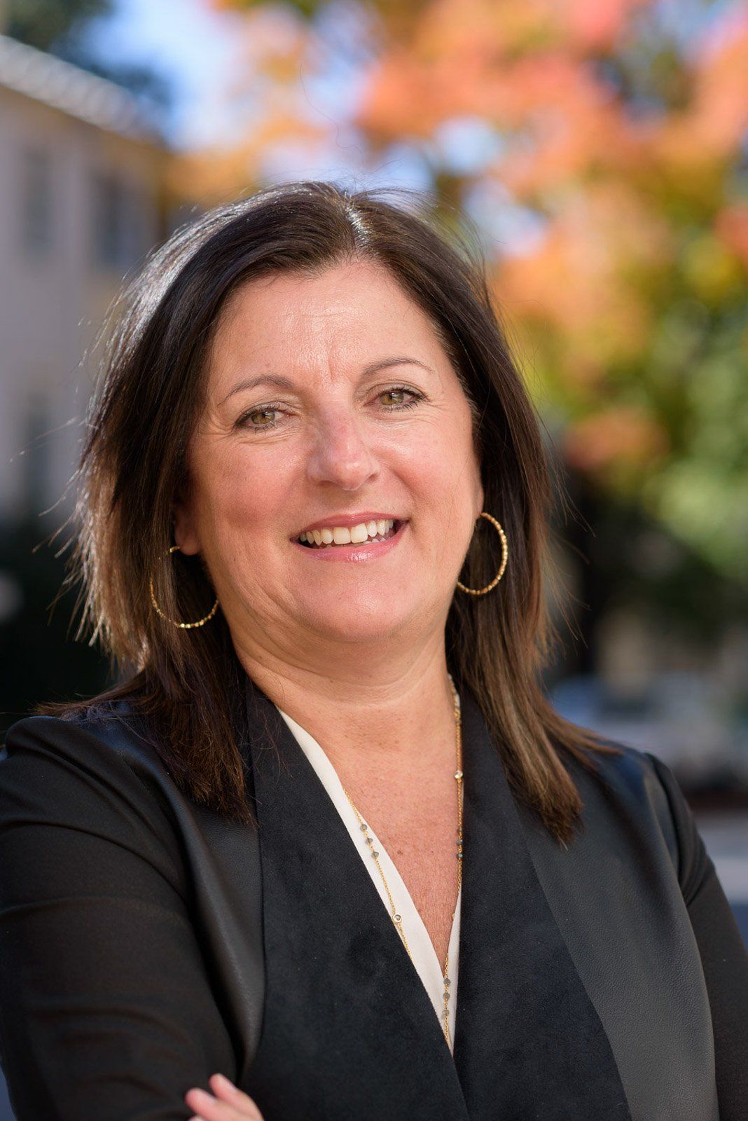 A woman in a black jacket and earrings is smiling for the camera.