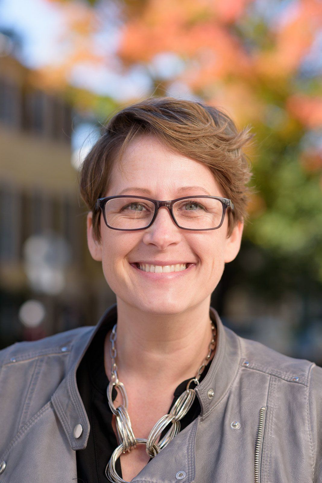 A woman wearing glasses and a necklace is smiling for the camera.
