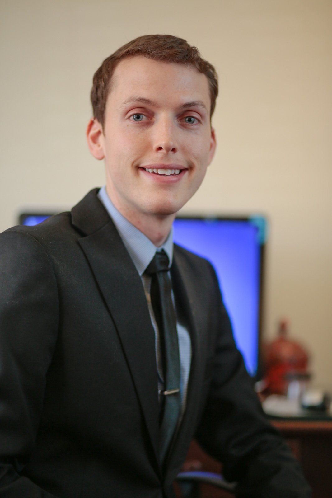 A man in a suit and tie is standing in front of a computer monitor.