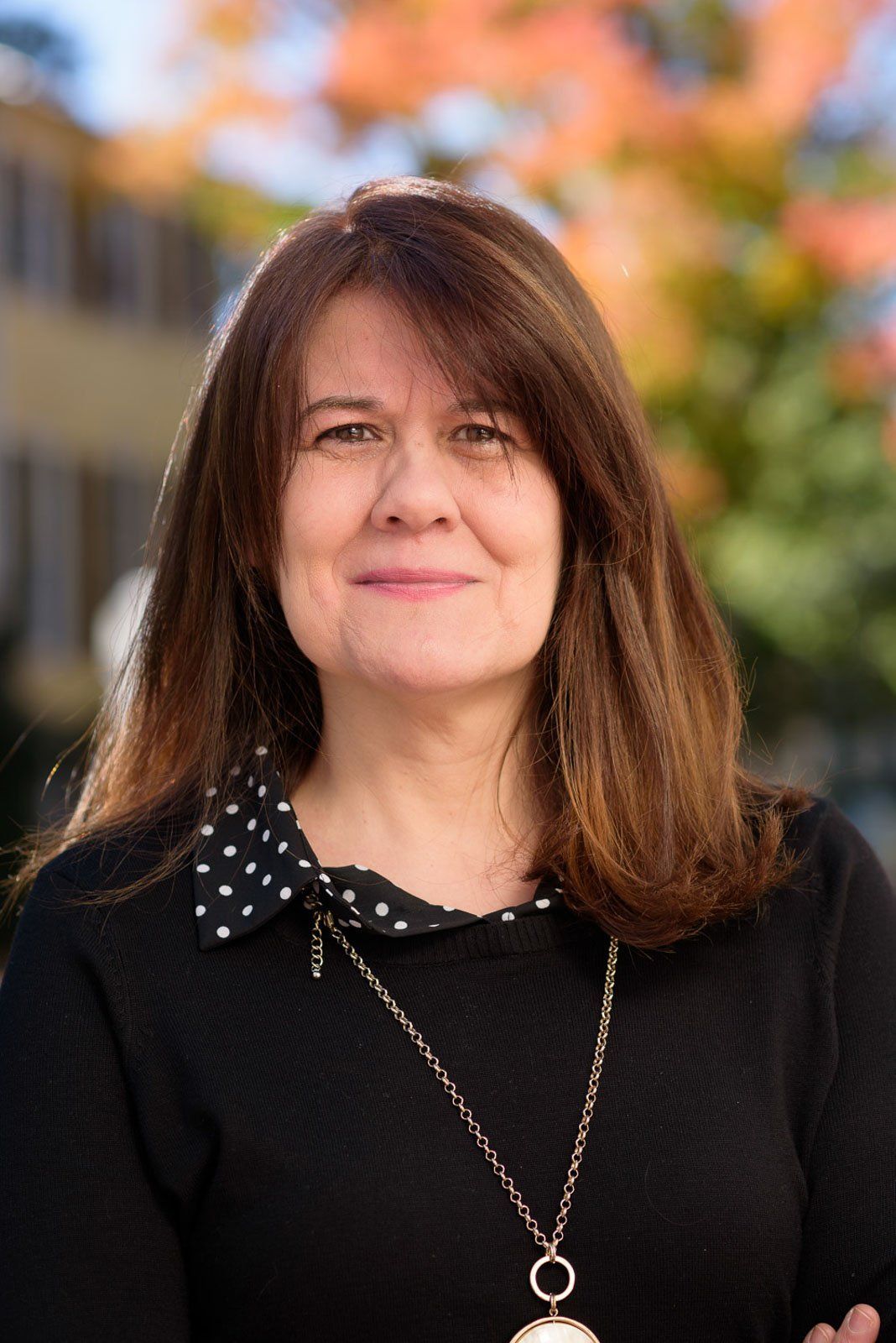 A woman wearing a black shirt and a necklace is smiling for the camera.
