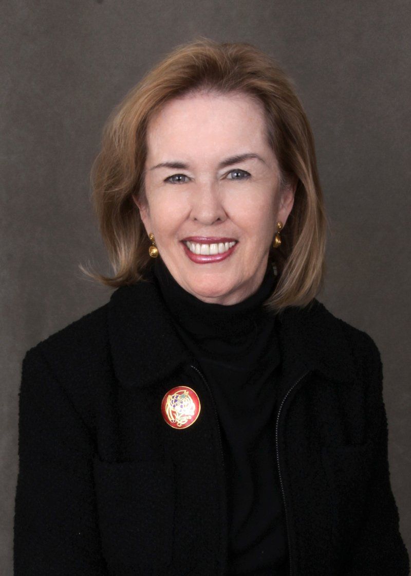 A woman wearing a black jacket and a brooch smiles for the camera