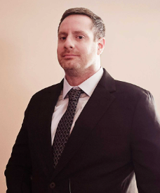 A man in a suit and tie is standing in front of a wall.