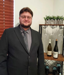 A man in a suit and tie stands in front of a wine rack