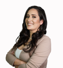 A woman with long dark hair is smiling with her arms crossed