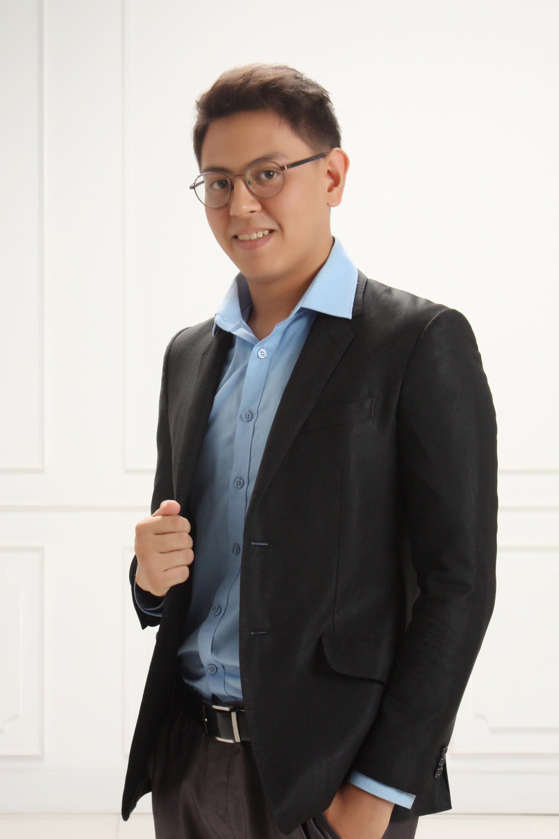 A man in a suit and glasses is standing in front of a white wall.