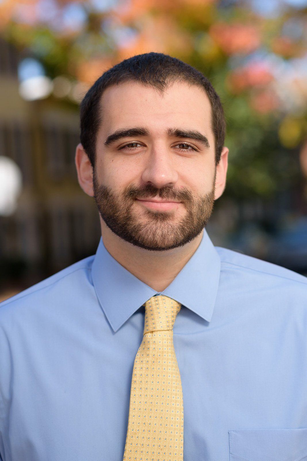 A man with a beard is wearing a blue shirt and a yellow tie.