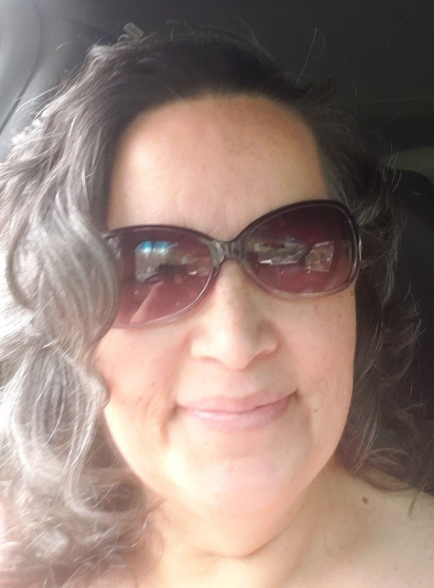 A woman wearing sunglasses is smiling while sitting in a car.