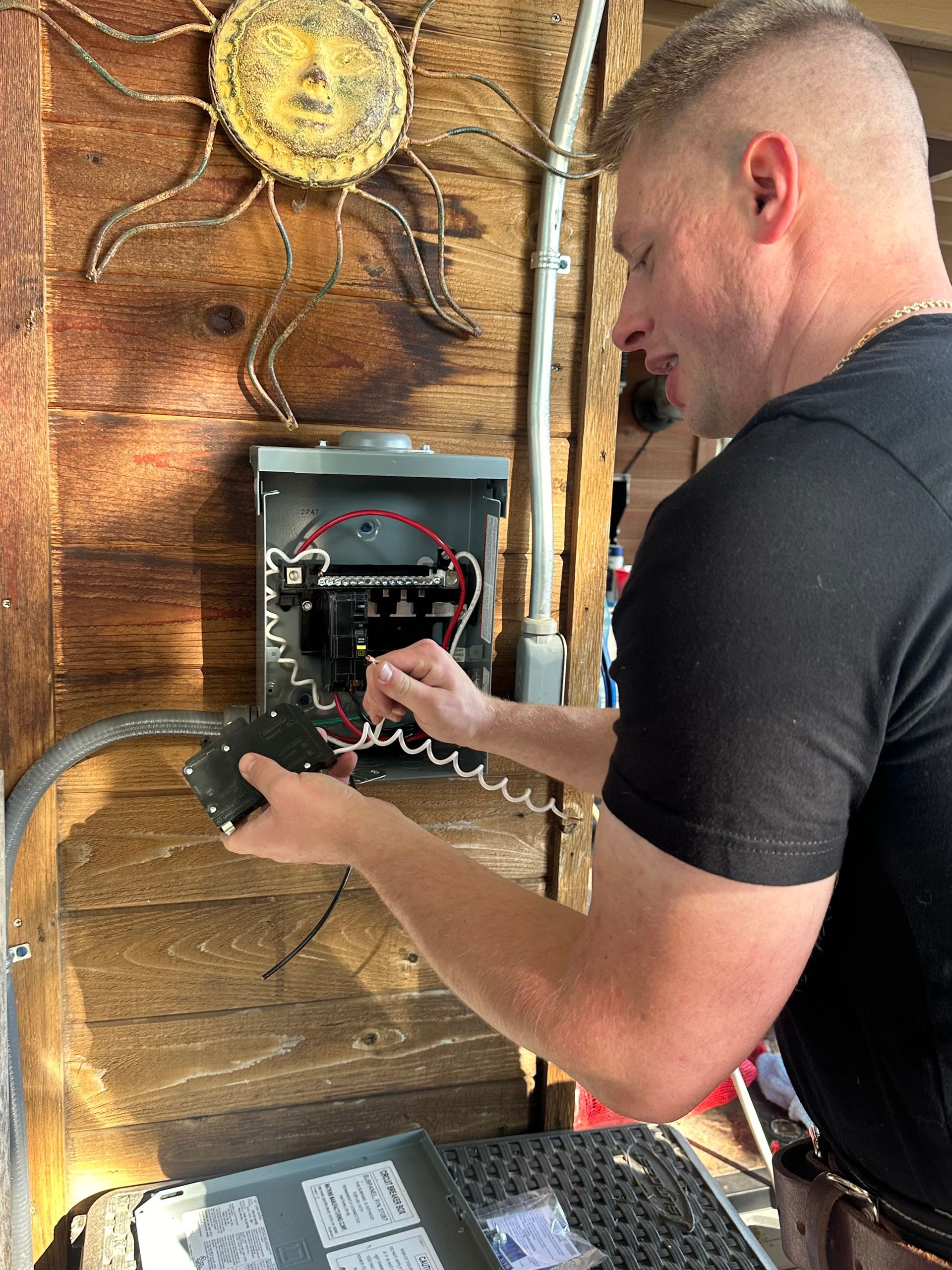 A man in a black shirt is working on an electrical box.