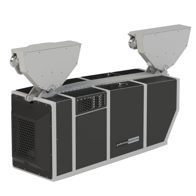 Macchina industriale con pannelli neri e grigi, due scivoli bianchi angolati e griglie di ventilazione.