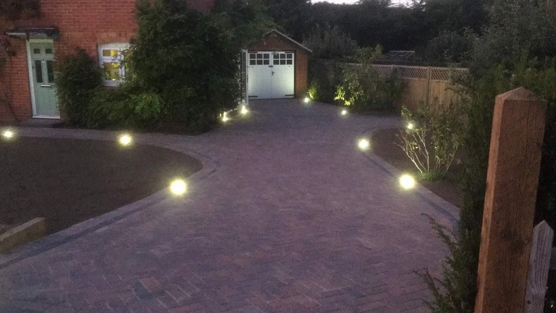A driveway leading to a garage is lit up at night.
