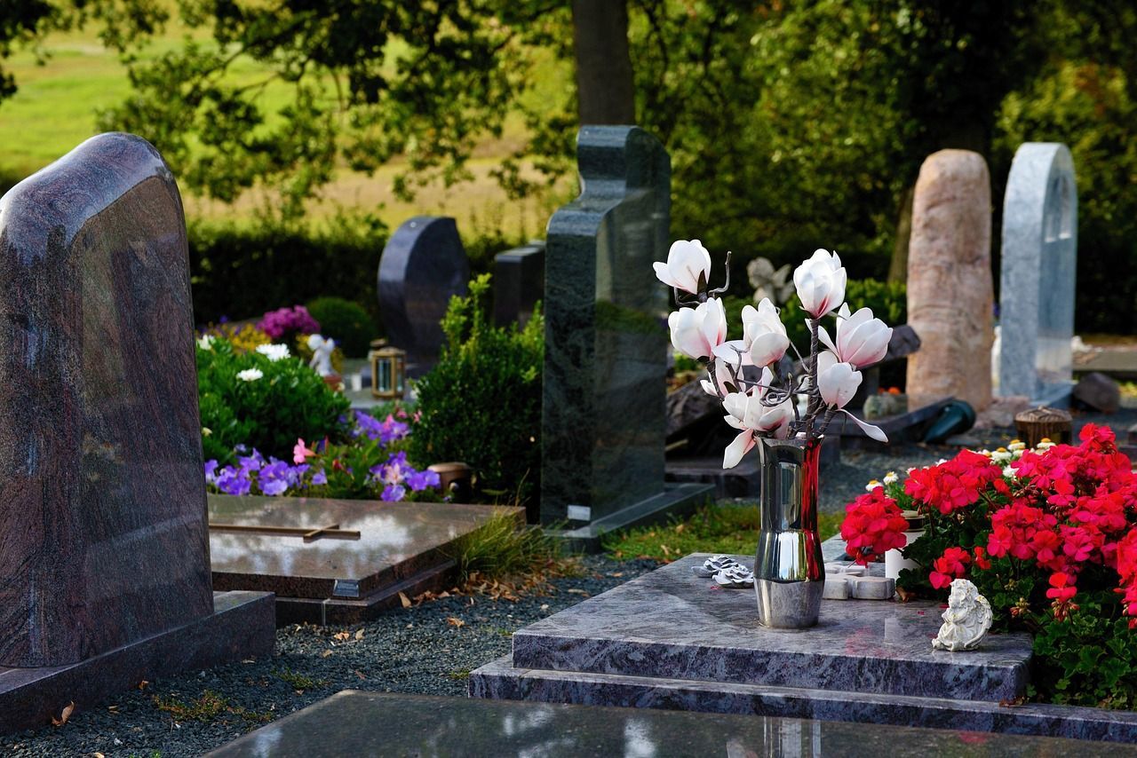 Photo of a cemetery, showing a few stone gravemarkers, with flowers on top