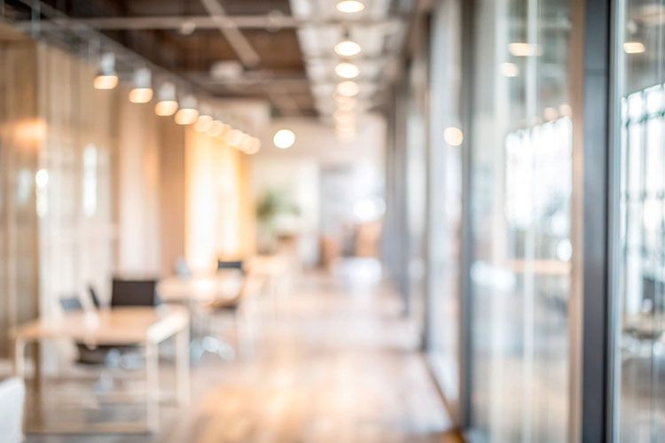 A blurry picture of a hallway in an office building with tables and chairs.