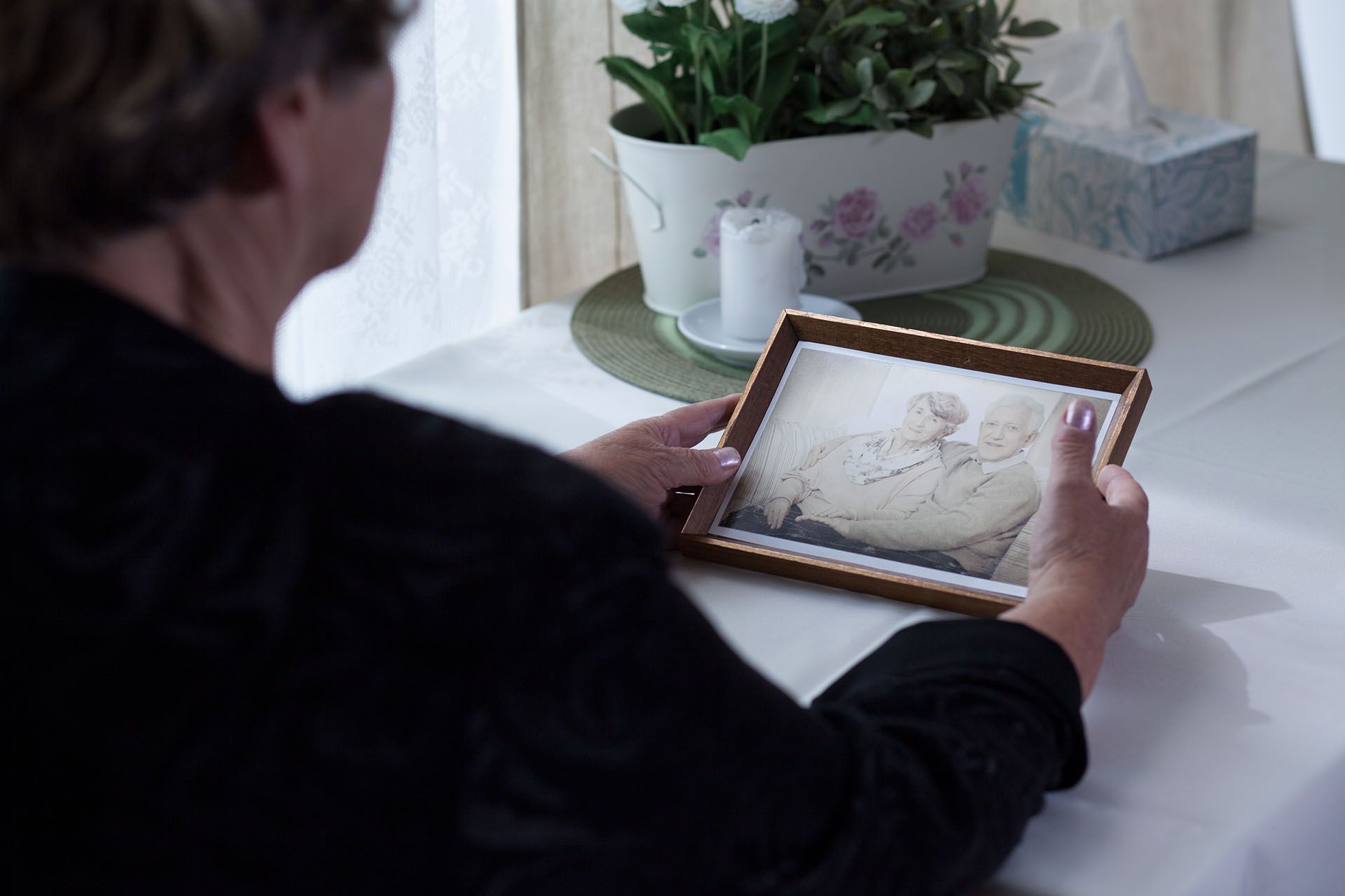 A woman is sitting at a table holding a framed picture of a man and woman.