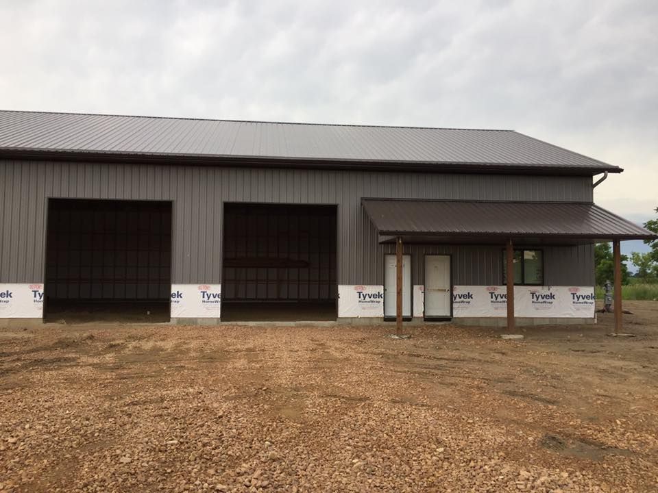 A large gray building with a brown roof and a porch.