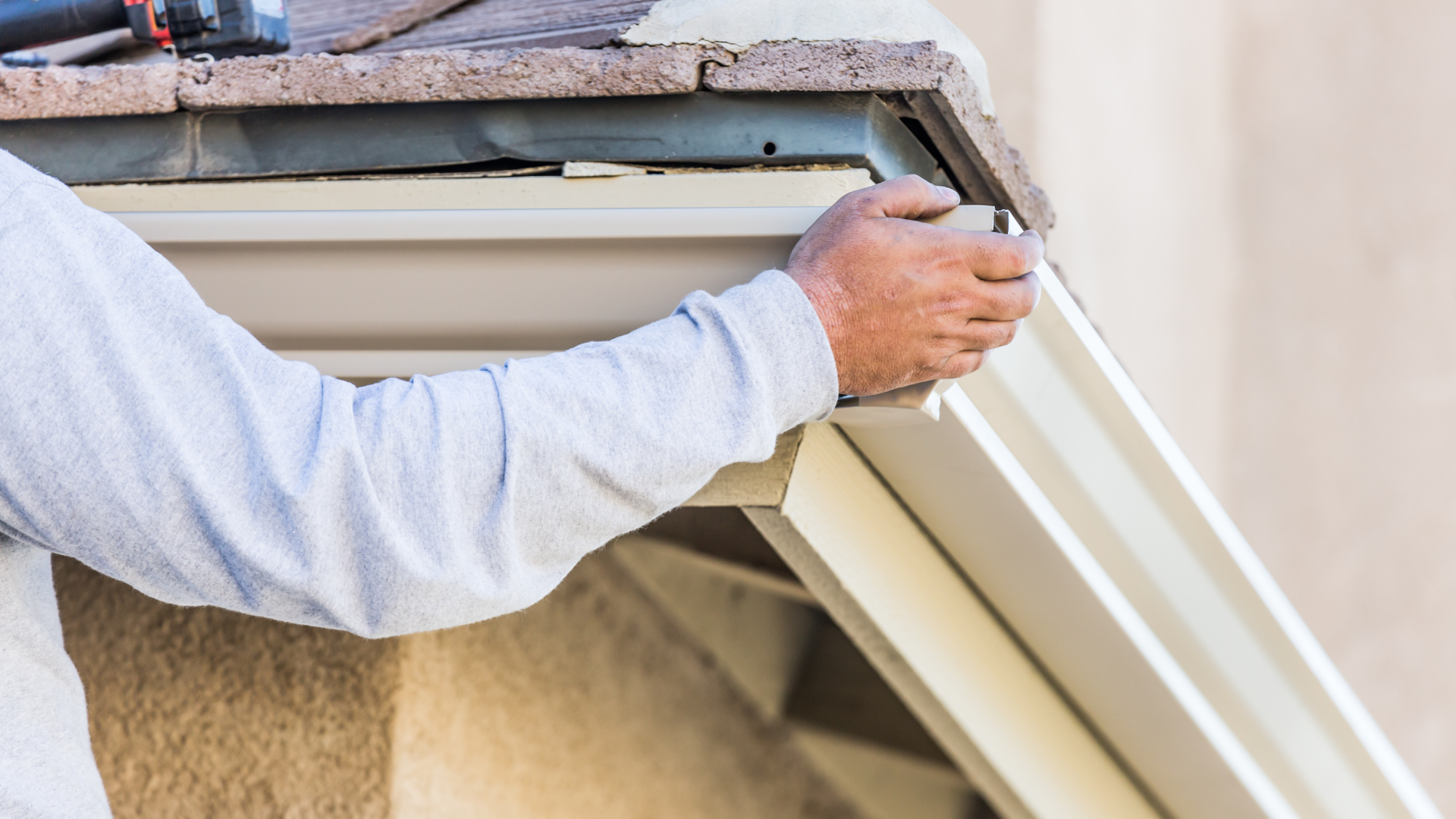 A man is installing a gutter on the side of a building.