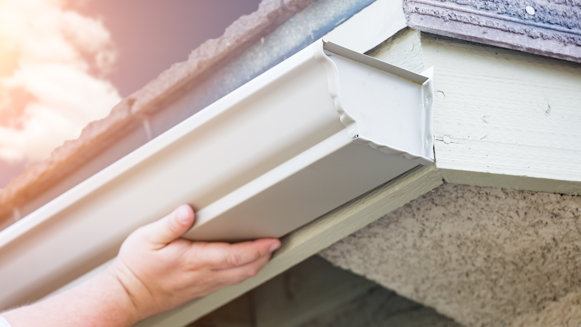 A person is installing a gutter on the side of a house.