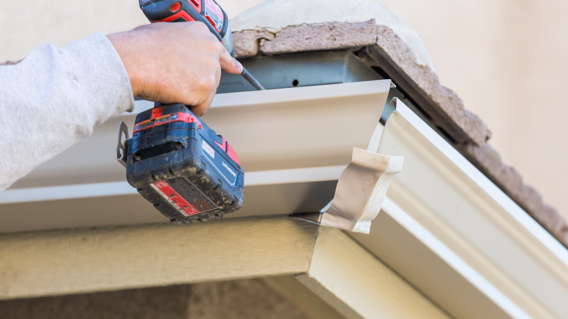 A man is installing a gutter on a roof with a cordless drill.