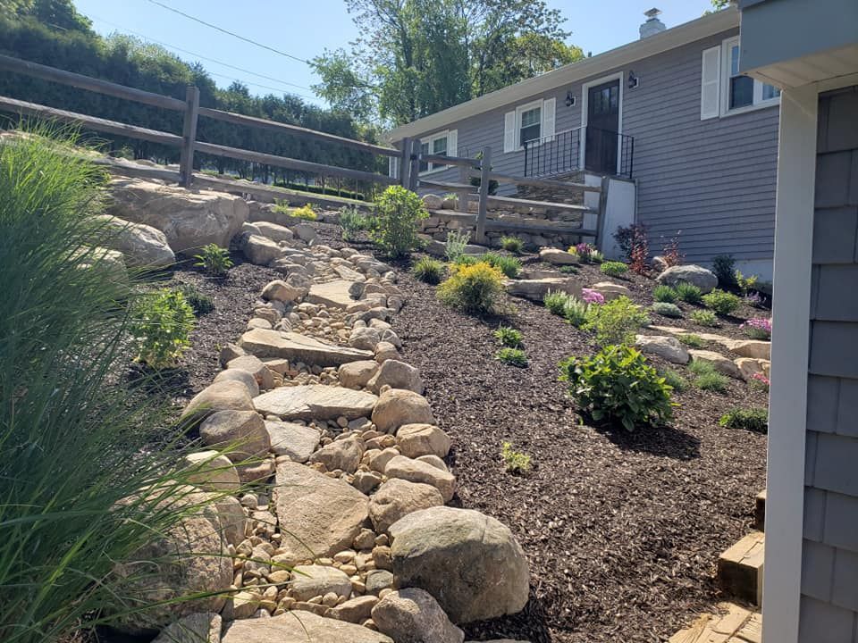 A rocky path leading to a house with a wooden fence in the background.