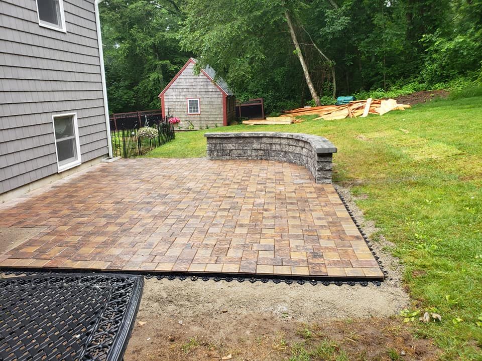 A brick patio is being built in the backyard of a house.