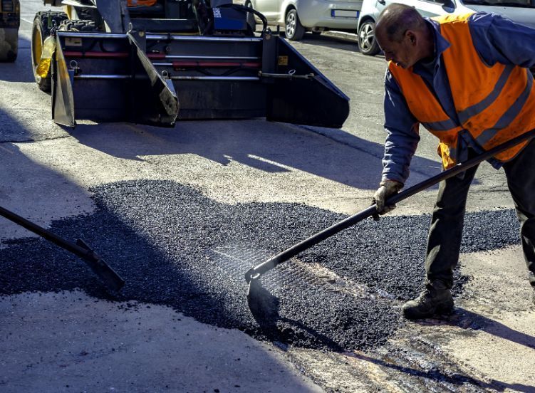 A man is Spreading Asphalt on the Ground with a shovel — Potholes ‘R’ Us In Toowoomba, QLD