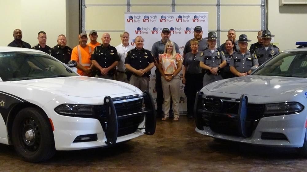 A group of police officers are posing for a picture next to two police cars.