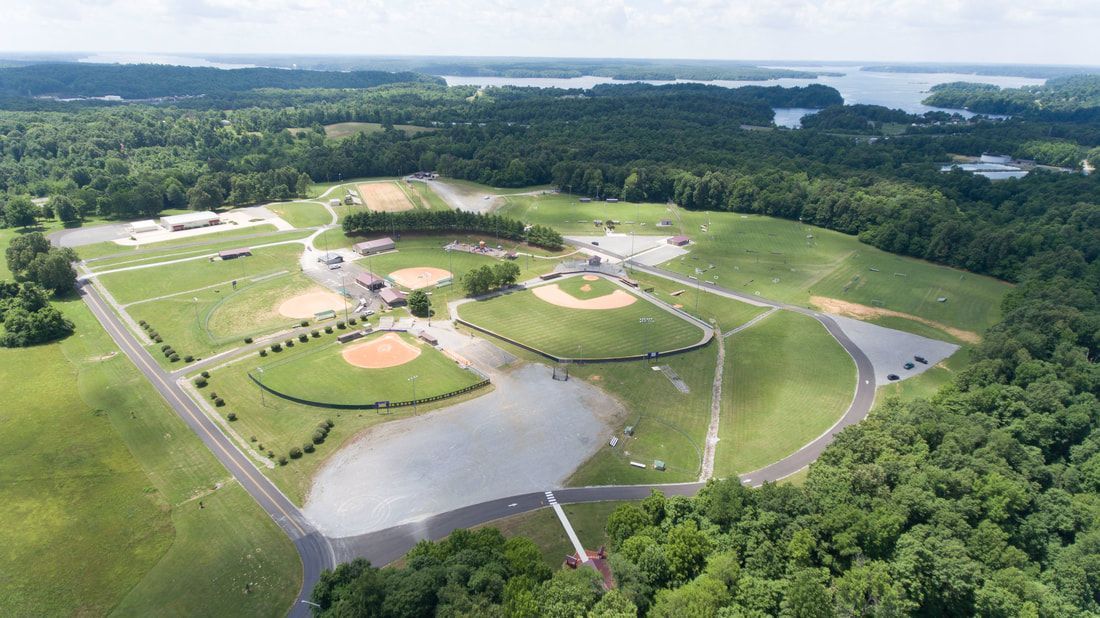 An aerial view of a baseball field surrounded by trees and a lake.