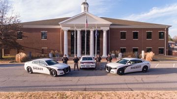 Three police cars are parked in front of a large brick building.