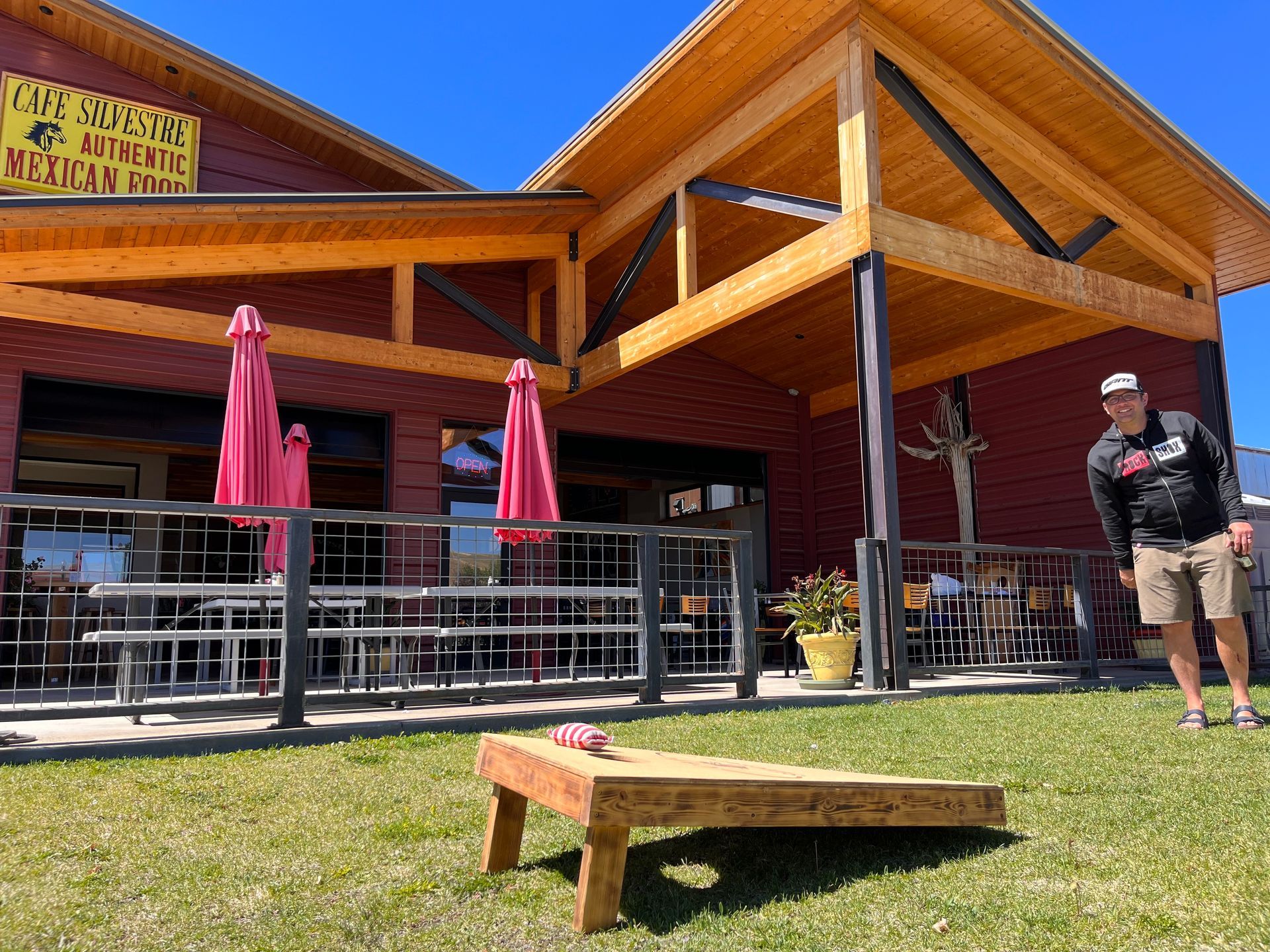 A man is playing a game of cornhole in front of a restaurant.