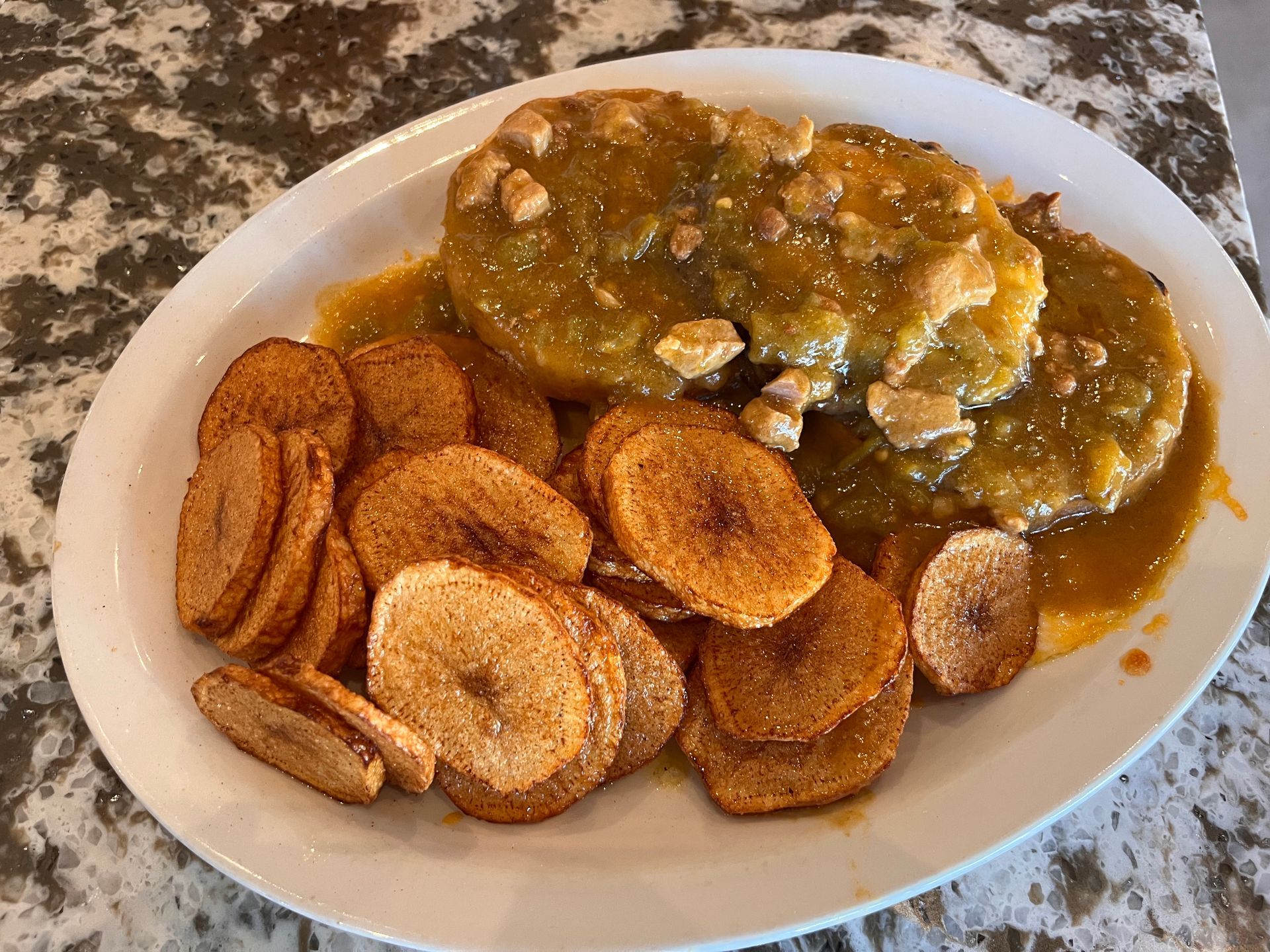 A white plate topped with chicken and plantains on a table.