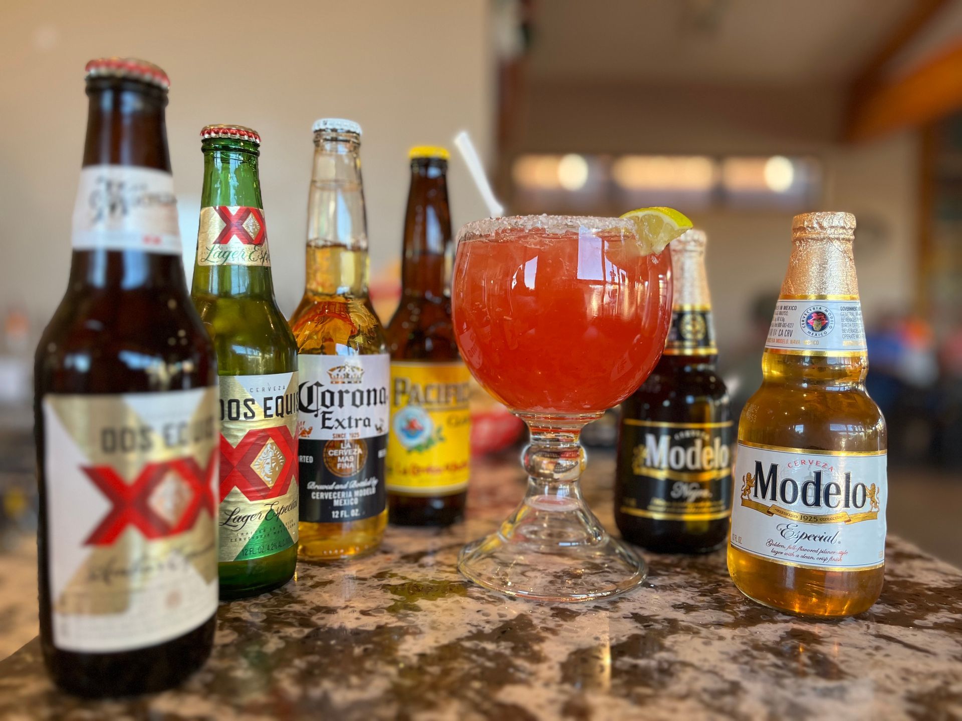 A row of beer bottles and a margarita on a table.