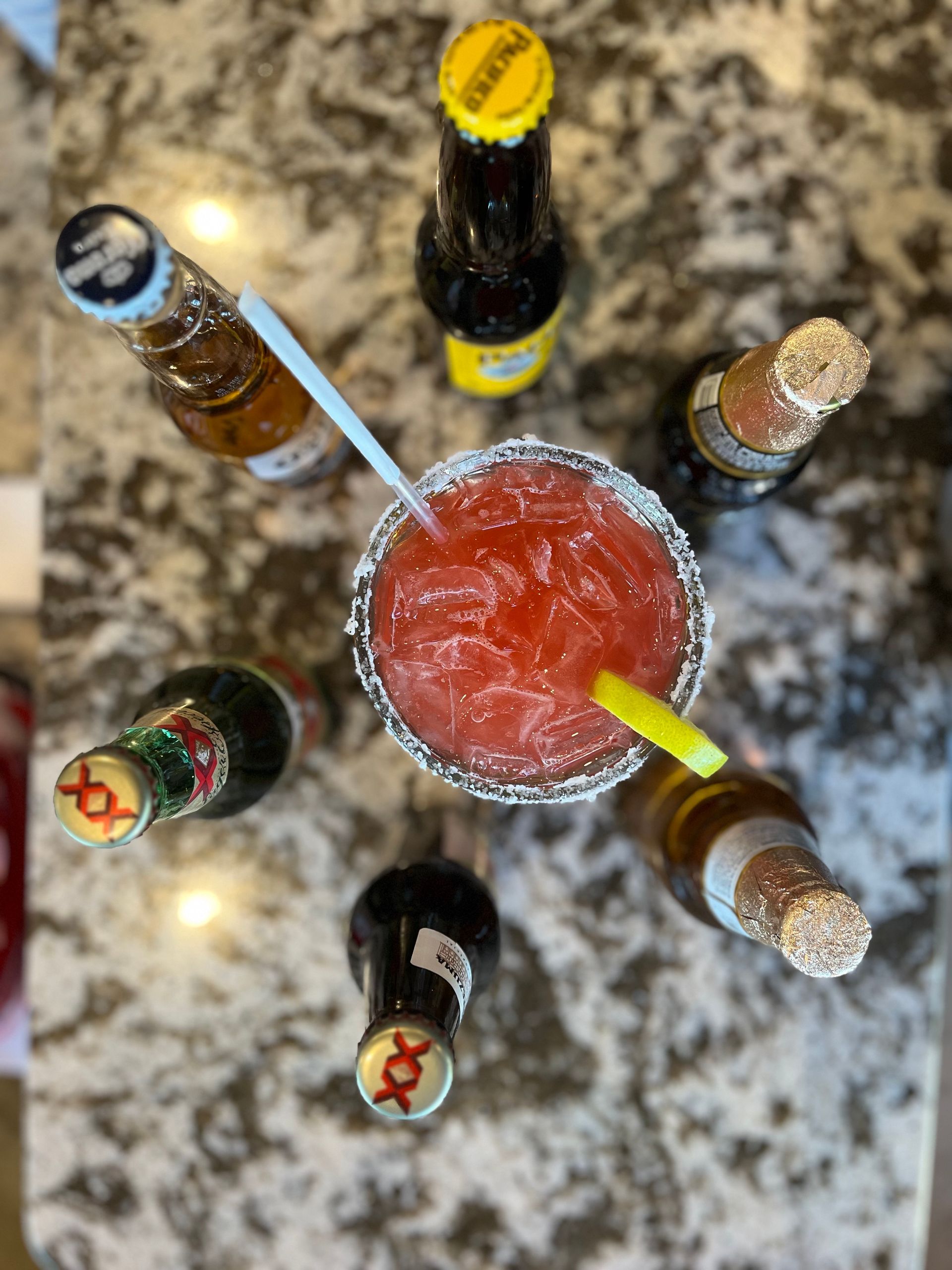 A margarita is surrounded by beer bottles on a counter.
