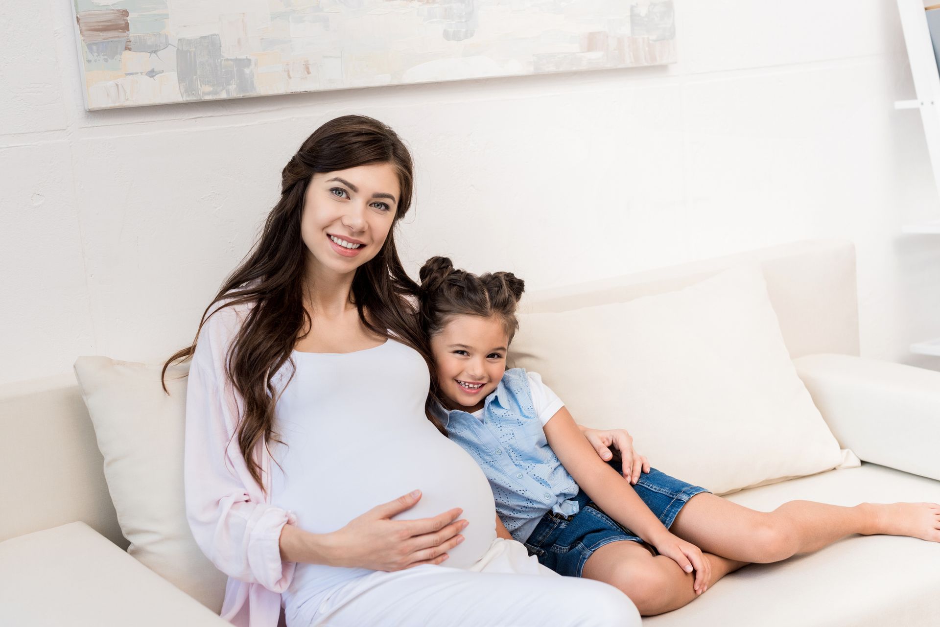 Pregnant mother and her child sitting on a sofa together