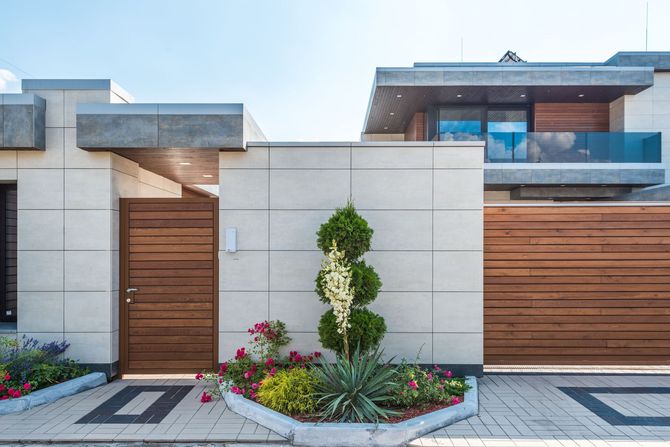 Modern house facade with wood garage door, front entry gate, and landscaped flower beds
