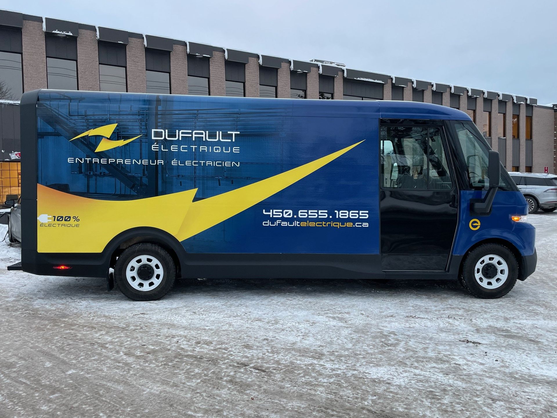 Une camionnette bleue et jaune est garée dans la neige devant un immeuble.