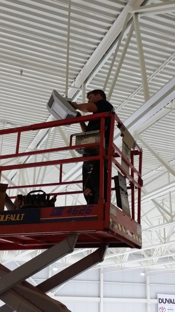 Un homme se tient debout sur un élévateur à ciseaux et travaille sur un luminaire.