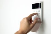 Hand entering a security code on a white keypad mounted on a white wall.