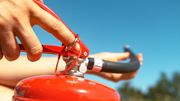 Person's hands activating a red fire extinguisher outdoors against a blue sky.