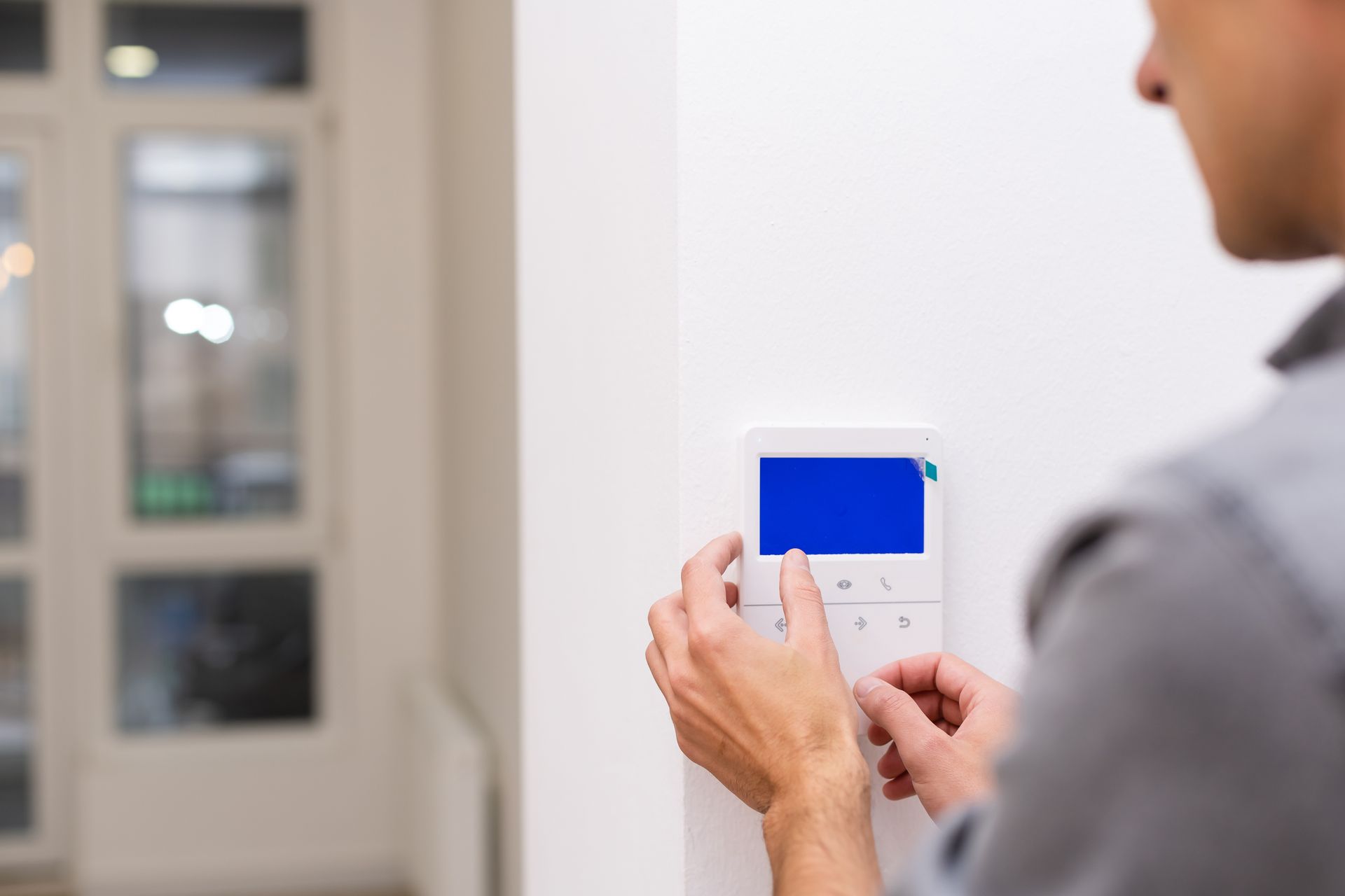 Person adjusts a thermostat on a white wall in a room with a window. The screen is blue.