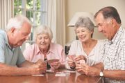 Four older adults seated at a table playing cards; smiling, in a well-lit room.