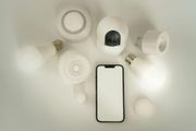 Smart home devices: Phone, camera, smart bulbs, plugs, and speakers on a white surface.
