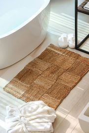 Bathroom with a white bathtub, woven bath mat, robe, and slippers.