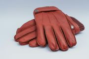 Leather gloves, rust-colored, with button detail, resting on a white surface.