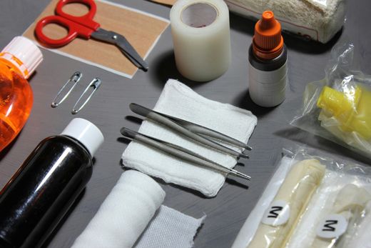 First aid kit contents: scissors, tape, gauze, antiseptic, bandages, and tweezers on a gray surface.